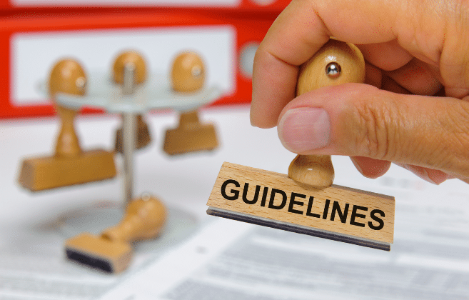 A hand holding a wooden rubber stamp with the word 'GUIDELINES' over a document, with blurred stamping tools in the background, signifying the importance of following guidelines, possibly in the context of end-of-lease procedures.