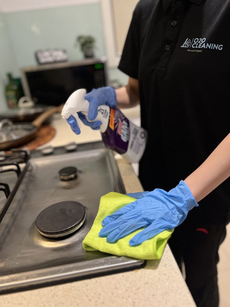 A professional from O2O Cleaning uses a cleaning spray and microfiber cloth to scrub a stovetop for a deep clean.