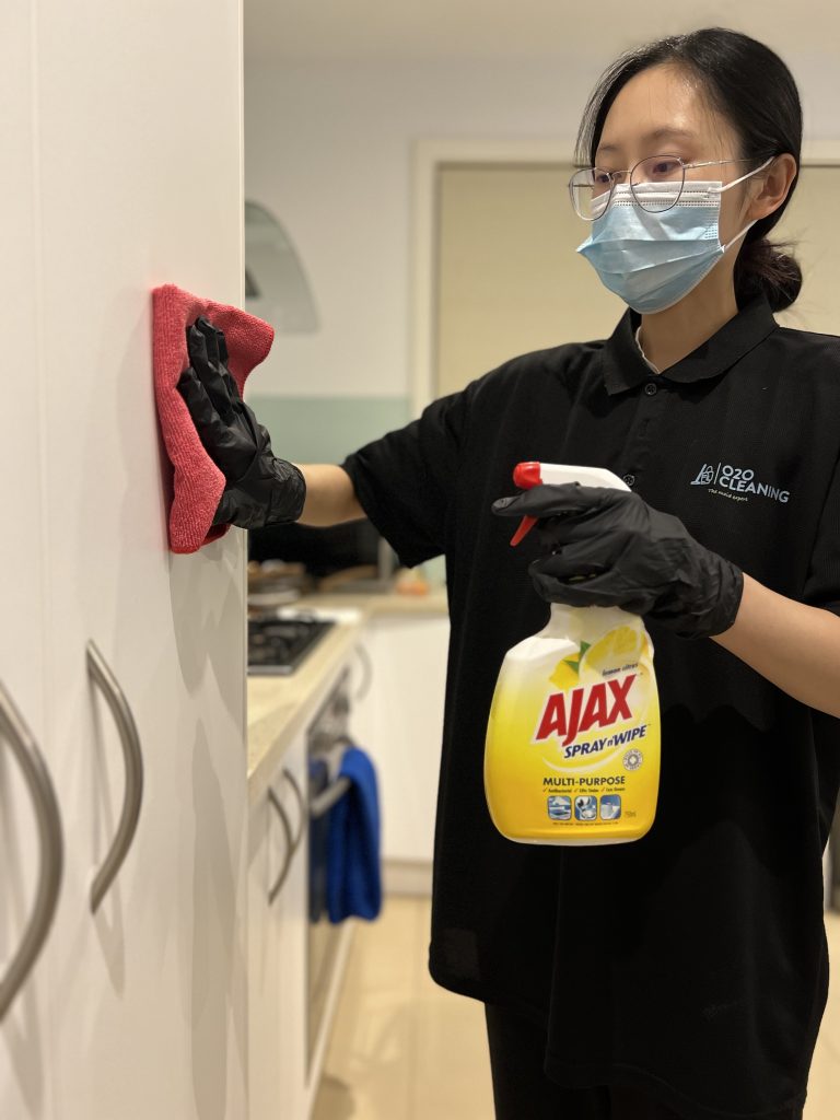 A professional cleaner spraying Ajax multipurpose cleaner on a kitchen cabinet while holding a sponge.