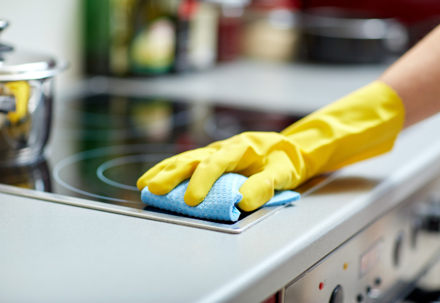 Person wearing yellow gloves cleaning a stovetop with a cloth
