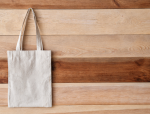 A reusable fabric shopping bag made from an old sheet hanging on a wooden wall.