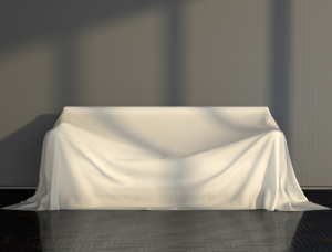 A couch covered with a white fabric sheet in a well-lit room.