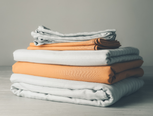 A stack of folded colorful bed sheets neatly arranged on a white surface.